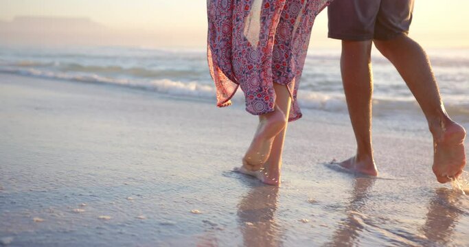 Biracial couple walks barefoot on the beach at sunset, woman wearing a patterned dress, with copy sp