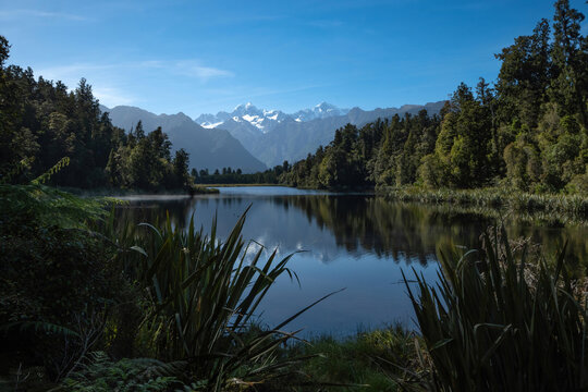A calm and peaceful Lake Matheson in the summer morning, with a beautiful reflection of Mount Tasman and Mount Cook in a lake water.