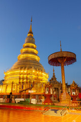 Naklejka premium Golden Buddhist stupa at Wat Phrathat Haripunchai Woramahawihan, Lamphun, Thailand, at dusk.