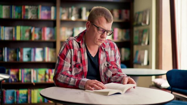 male professor in glasses sits in a scientific and technical library reads a book and prepares write a dissertation