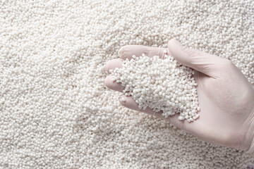 Close-up of a man's hand in a protective glove holds a lot of white plastic polymer granules.