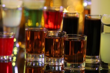 Different shooters in shot glasses on mirror surface against blurred background, closeup. Alcohol drink