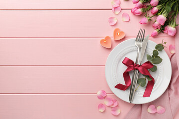 Place setting with heart shaped candles and bouquet of roses for romantic dinner on pink wooden table, flat lay. Space for text