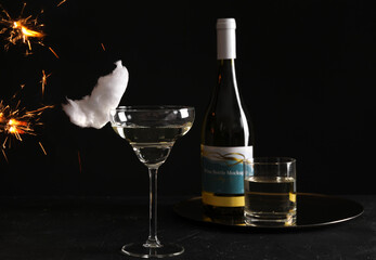 Cocktail with tasty cotton candy and bottle of alcohol drink on dark textured table