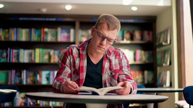 male professor in glasses sits in a scientific and technical library reads a book and prepares write a dissertation