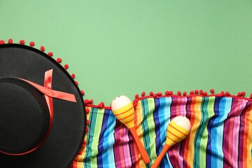 Mexican sombrero hat, maracas and colorful poncho on green background, flat lay. Space for text