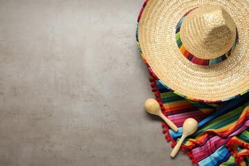 Mexican sombrero hat, maracas and colorful poncho on grey textured background, flat lay. Space for...