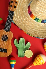 Flat lay composition with Mexican sombrero hat and ukulele on red background