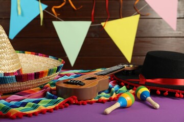 Mexican sombrero and black Flamenco hats, ukulele and maracas on purple table, closeup