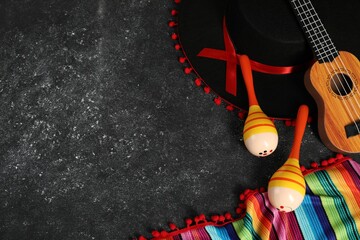 Black Flamenco hat, ukulele, poncho and maracas on dark textured table, flat lay. Space for text