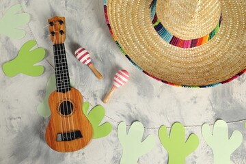 Mexican sombrero hat, ukulele and maracas on grey textured table, flat lay