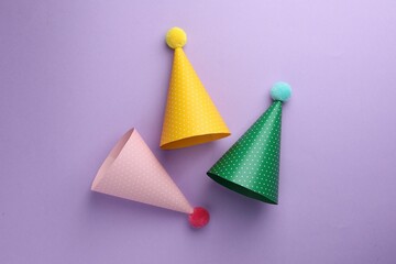 Beautiful party hats on purple background, top view