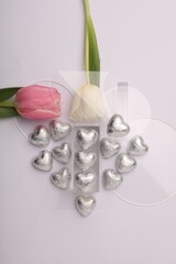 Heart made with delicious chocolate candies and beautiful tulips on white background, top view