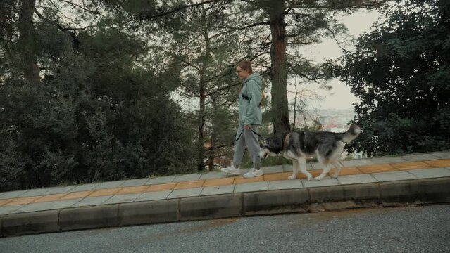 Active casual young woman walking with Husky dog autumn urban park asphalt