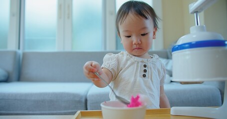 Adorable toddler skillfully using a spoon during self-feeding at a home, a milestone in child development