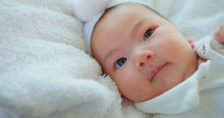 A contented baby with sparkling eyes and a soft headband lies on a plush fluffy white blanket, exuding warmth innocence and comfort