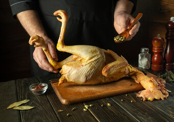 Adding spices with a spoon to raw chicken. The chef is preparing a rooster on the kitchen table for...