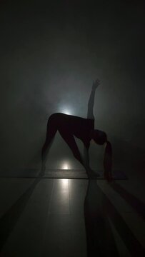 Silhouette of woman exercising and practicing balance with yoga pose in gym with steam. Healthy lifestyle, fitness and mindfulness