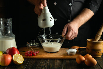 A professional chef prepares milk yogurt with fruit. Hand electric mixer in the hand of a cook. Low...