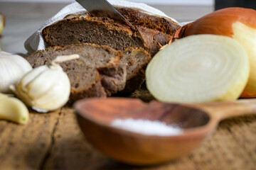 bread placed on a cloth with a knife, garlic, onion, salt and a wooden spoon on a wooden background
