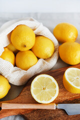 Whole and sliced ​​lemons on a wooden board next to a knife on a light background