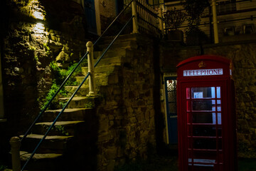 Street corner in the historical town of Rye, with a red telephone box, Image shows a small open area at night illuminated by street lighting with traditional stone building in the background.