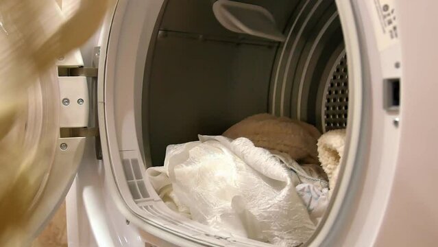 The open door of the electric dryer, a man's hand takes out the dried laundry.