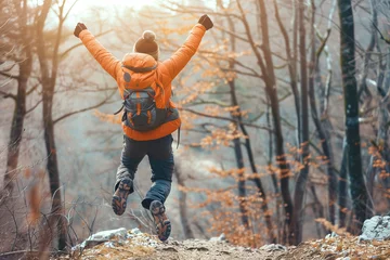 Foto op Aluminium  Happy man with arms up jumping on the top of the mountain - Successful hiker celebrating success on the cliff - Life style concept with young male climbing in the forest pathway © gilles