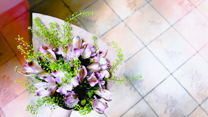 Purple Alstroemerias flowers wrapped in craft paper against tiled floor. Floral composition background with copy space. film grain pixel texture. soft focus. blur.