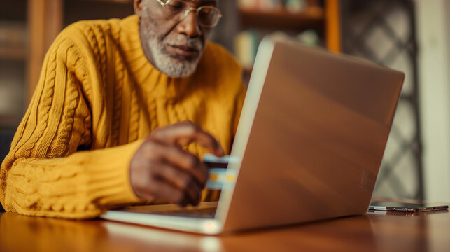 Elderly African American man enters his credit card information online using his laptop connected to the internet. Senior people vulnerable to online scams