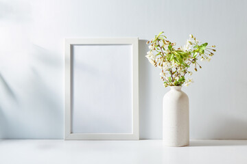 Mockup with a white frame and spring flowers in a vase on a light background. Empty poster frame mockup for presentation design, text, lettering