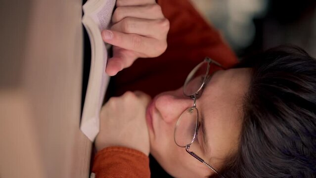 vertical video close-up male sits in scientific and technical library reads a book and prepares write a dissertation