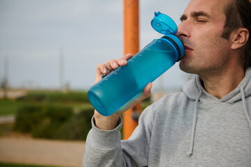 Close-up sportswoman, male athlete drinks water to hydrate body after outdoor cardio workout.