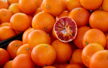 backdrop of many ripe oranges and one cut open to reveal the juice on sale at a market in a Mediterranean country - obrazy, fototapety, plakaty
