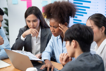 Diverse businesspeople analyzing financial dashboard data on laptop in serious meeting, confused...