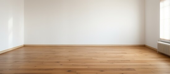 A room with laminate flooring and a white wall contains only a radiator and a window. The room appears bare and unoccupied, with a simple and minimalistic design.