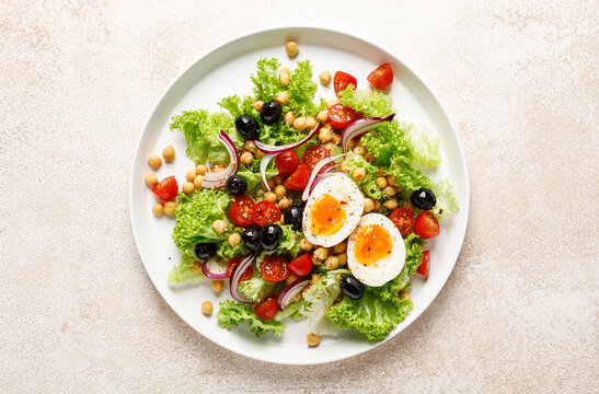 Soft-boiled egg Easter fresh vegetable salad with tomatoes, chickpea, olives, onion and green lettuce. Healthy food,  breakfast. Top view