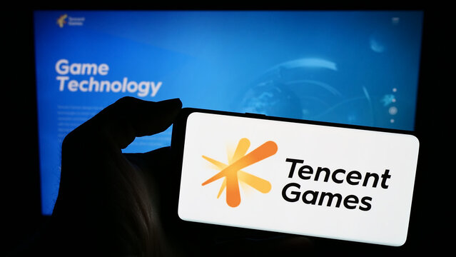 Stuttgart, Germany - 02-22-2024: Person holding mobile phone with logo of Chinese video game company Tencent Games in front of business web page. Focus on phone display.