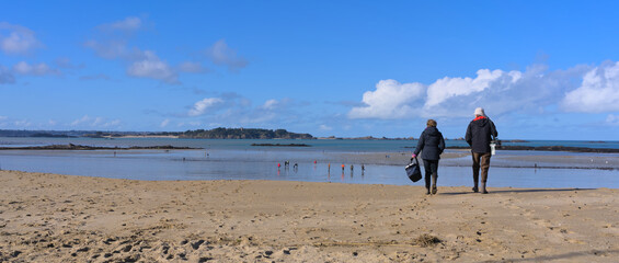 Two people going down sand beach of Lancieux, France during low tide