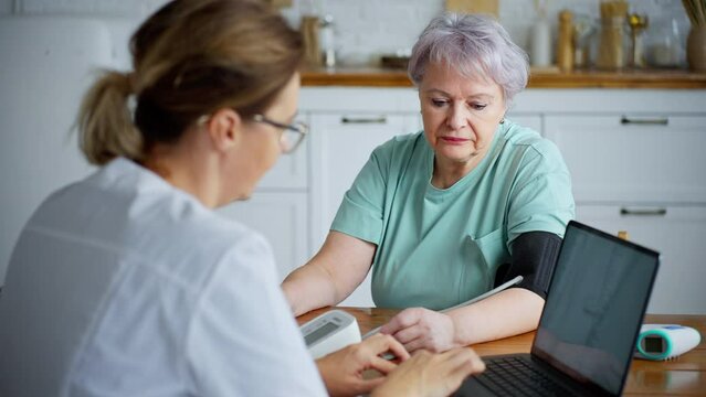 Healthcare worker monitors senior woman's blood pressure at home
