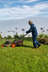 Yard worker mowing grass with lawn mower in garden. Lawn maintenance.