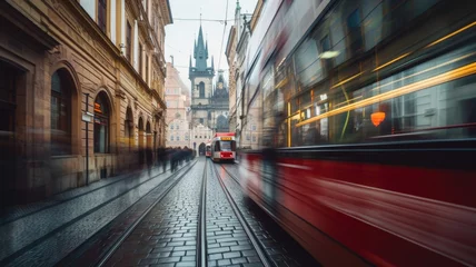 Fotobehang Dynamic image capturing the blur of a red tram in motion on cobblestone streets, with the iconic Gothic towers of Prague in the background on an overcast day. © Anna