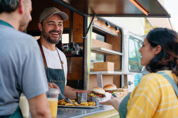 Candid shot of a male food truck owner engaging with customers while serving delicious street food, embodying authentic small business spirit and entrepreneurship.
