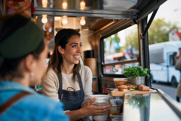 Candid shot of a female food truck owner engaging with customers, serving delicious food, embodying authentic small business spirit and entrepreneurship.

 - obrazy, fototapety, plakaty