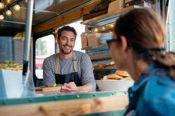 Candid shot of a male food truck owner engaging with customers while serving delicious street food, embodying authentic small business spirit and entrepreneurship.

