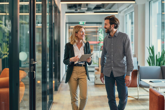 Male and female business colleagues engage in a positive conversation while walking through a contemporary office space, embodying teamwork and professionalism.

