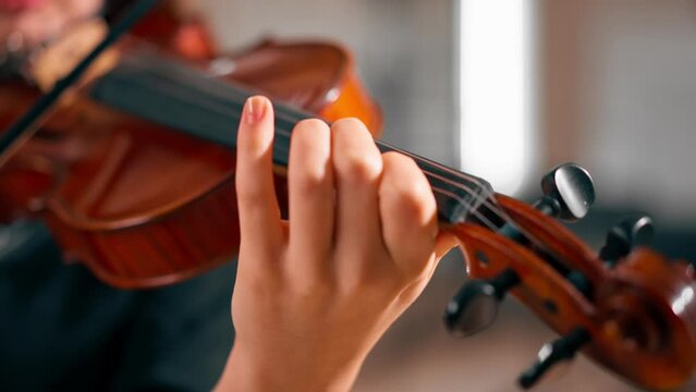 Close-up of a girl holding a violin with her fingers fingering the strings to perform classical musical composition