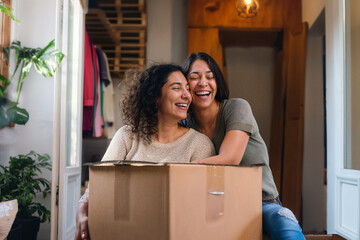 Lesbian couple joyously moving into their new home surrounded by boxes, embodying excitement and endless possibilities of authentic LGBTQ love.