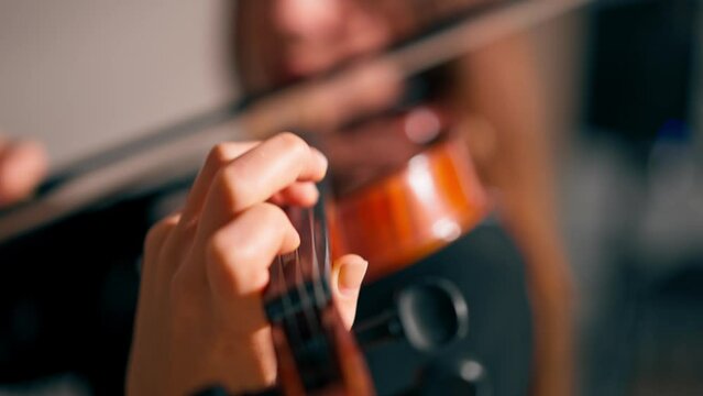 Close-up of a girl holding a violin with her fingers fingering the strings to perform classical musical composition