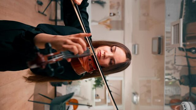 vertical video A girl violinist rehearses the melody of a classical piece of music on the violin in a music center at a rehearsal